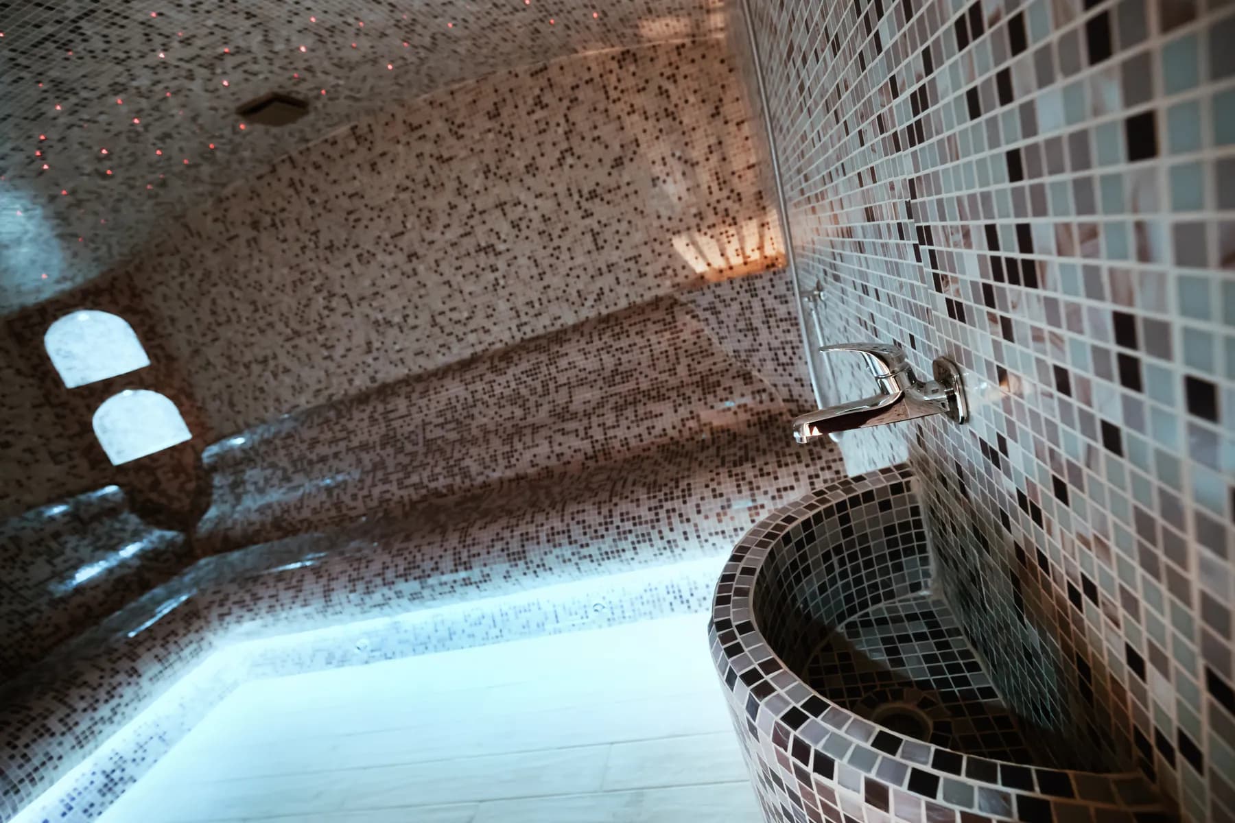 Mosaic steam room with a basin and lit benches