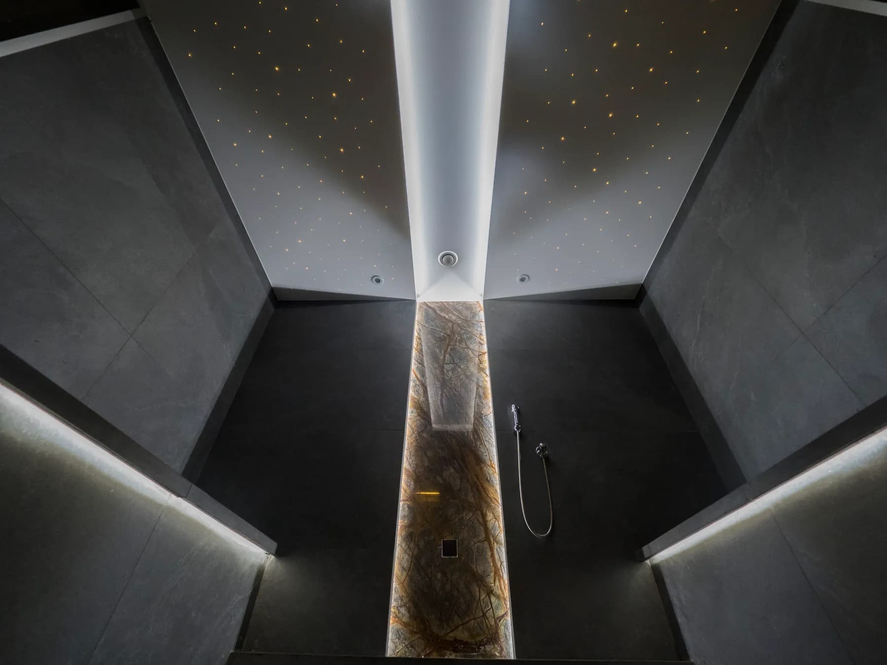 Steam room lined in black stone with a strip of light