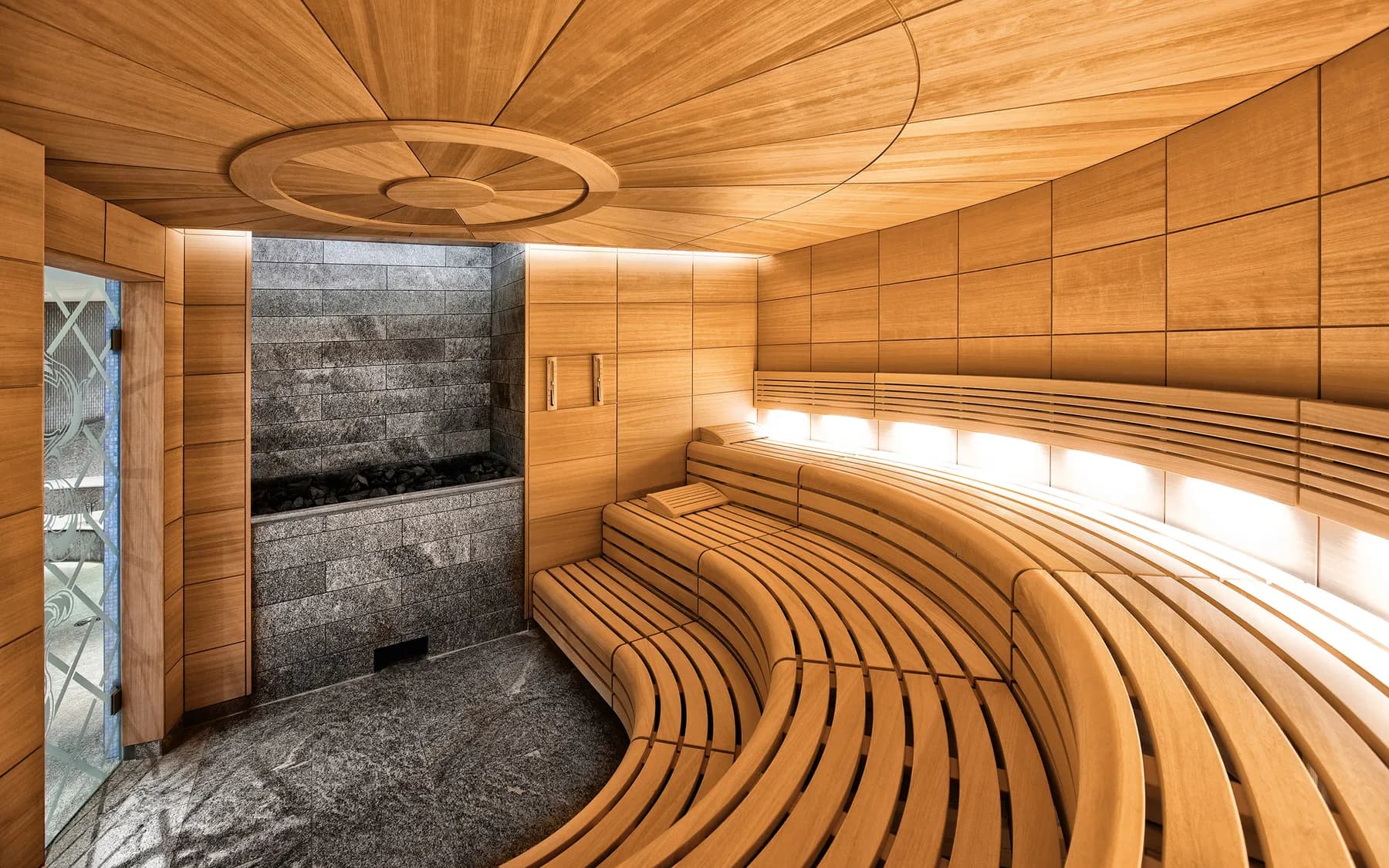 Sauna en bois aux banquettes courbes et mur en pierre