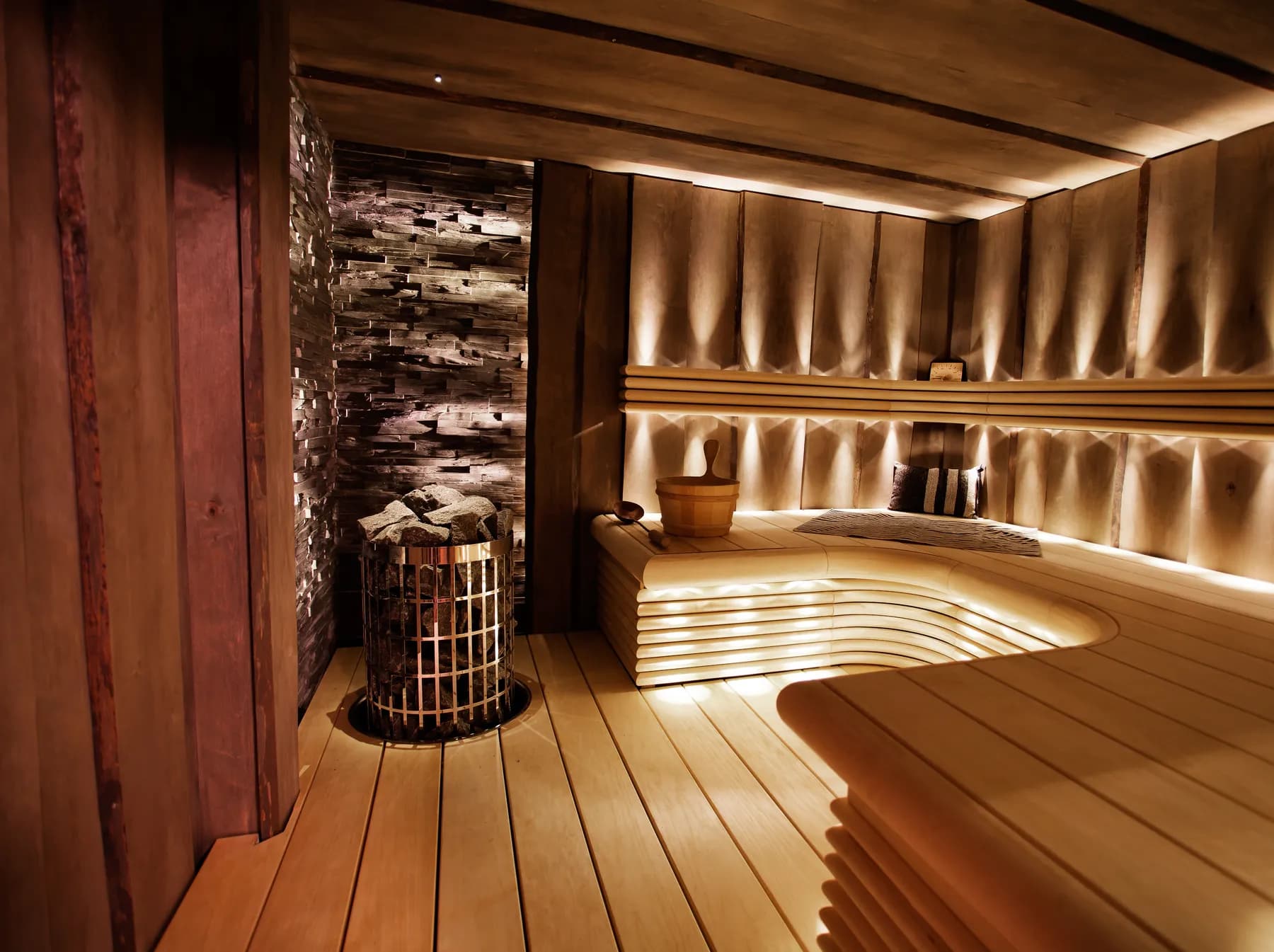 Sauna with a stone-clad heater wall and lit benches