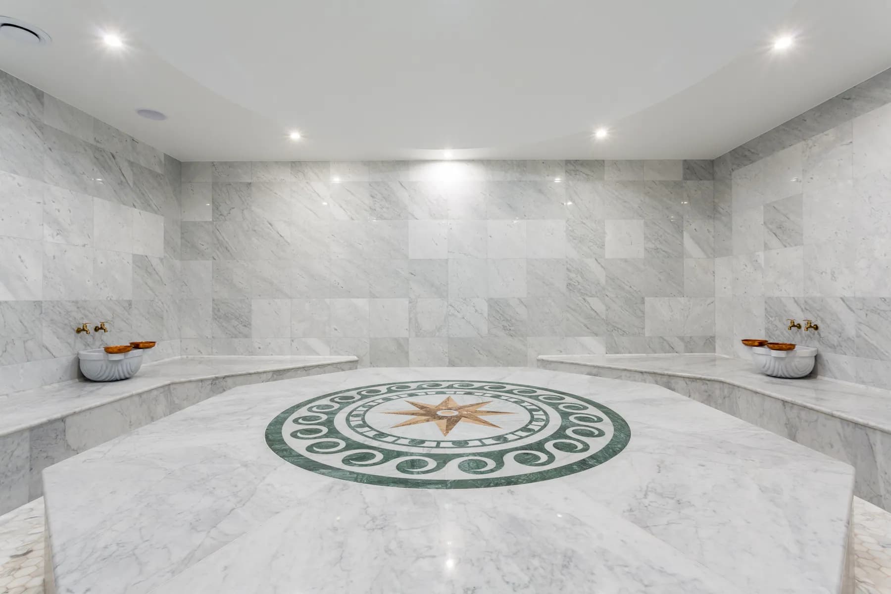 Hammam en marbre blanc au sol incrusté d'une étoile et vasques